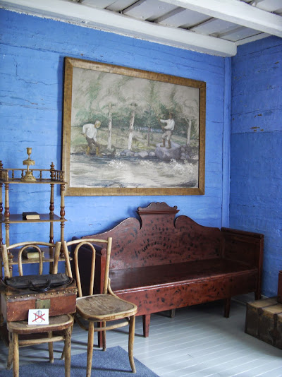 Vanhoja huonekaluja sinisessä huoneessa. Seinällä suuri taulu. 